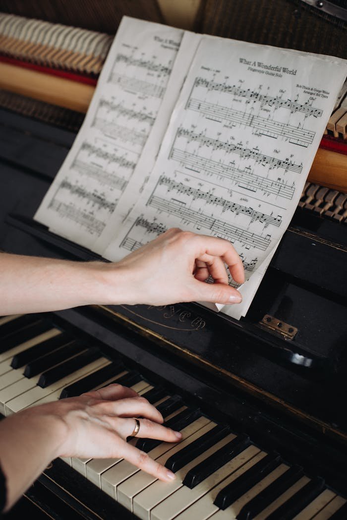 Close-up of a woman's hands on a piano, turning sheet music pages, capturing musical focus.